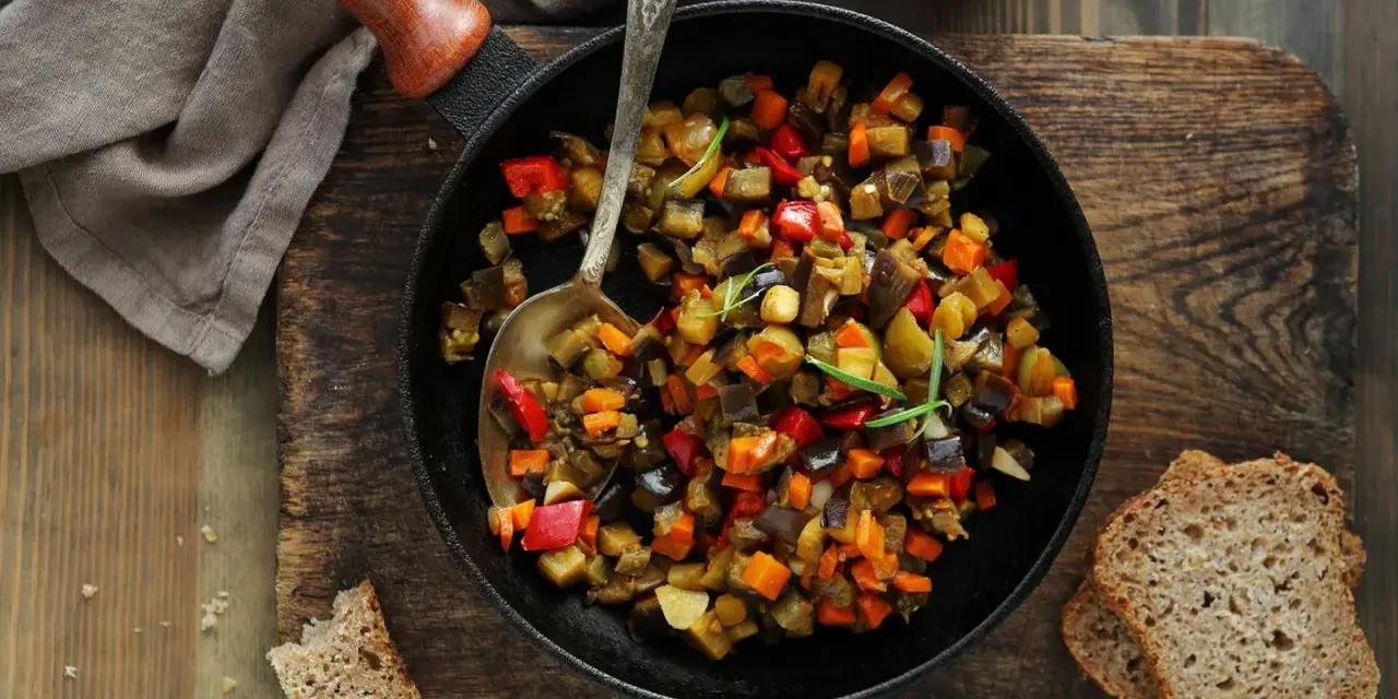 Ratatouille rezept: Buntes Gemüse aus Aubergine, Paprika und Karotten in einer Pfanne, serviert mit Brot.