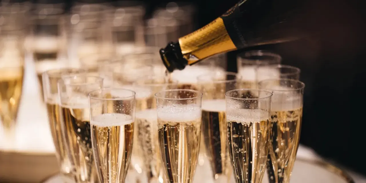 Sekt wird in Gläser gefüllt, die auf einem Tablett stehen. Die Bläschen steigen auf und erinnern daran, woher Champagner kommt.
