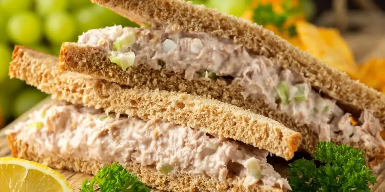 Zwei Tramezzini mit Thunfischsalat, Sellerie und Zwiebeln auf Vollkorntoast. Dazu Trauben, Zitrone und Petersilie. Perfekt für schnelle Tramezzini Rezepte.