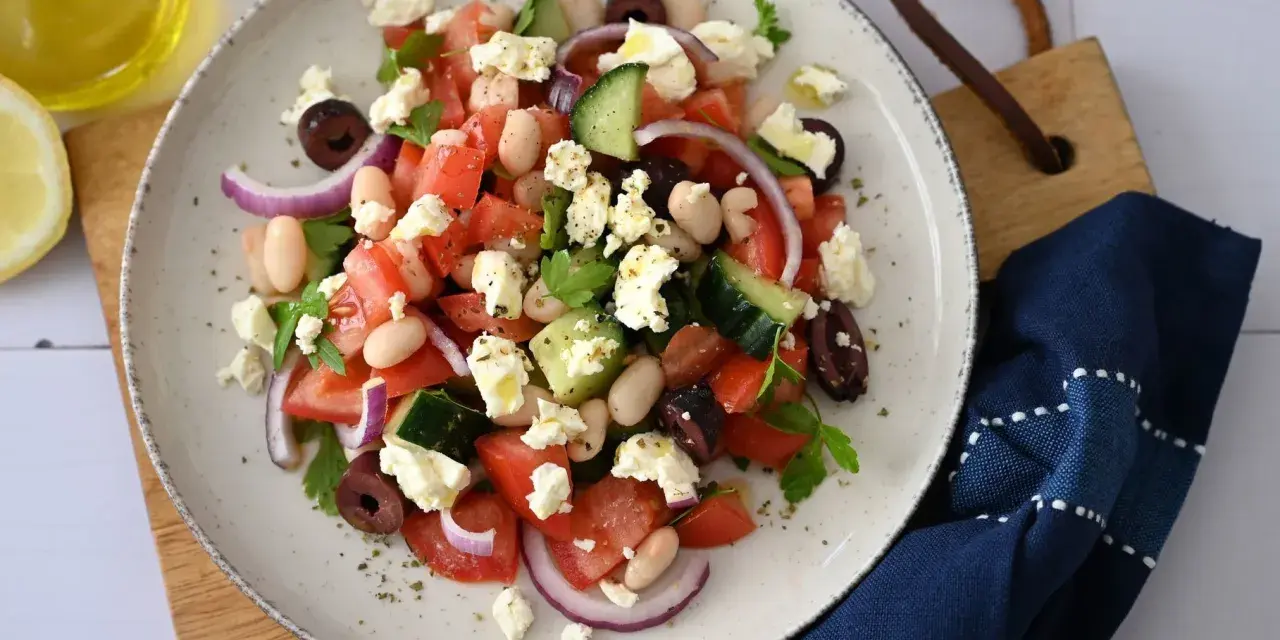 Frischer griechischer Bohnensalat mit Tomaten, Gurken, roten Zwiebeln, Oliven und Feta. Ein Spritzer Olivenöl und Zitrone machen ihn perfekt.