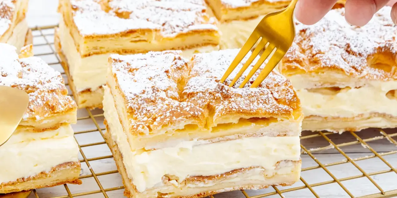 Ein goldener Löffel sticht in ein Stück polnischer Puddingkuchen, bestäubt mit Puderzucker.