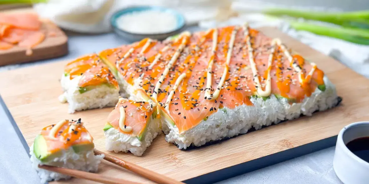 Rechteckiges Sushi mit Lachs und Avocado, verziert mit Mayonnaise und Sesam. Perfekt, um Sushi selber machen zu lernen!