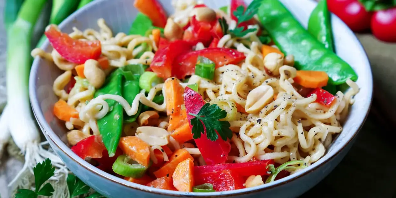 Bunter mie nudelsalat mit Erdnüssen, Zuckerschoten, Karotten und Paprika, garniert mit Petersilie.