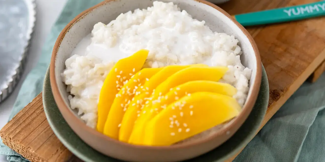 Schüssel mit cremigem **sticky rice** und saftigen Mangoscheiben, bestreut mit Sesam. Ein köstlicher Genuss!