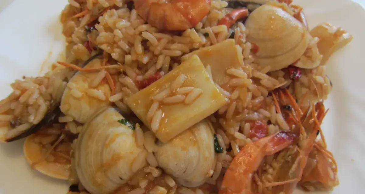 Ein köstlicher arroz de marisco mit Garnelen, Muscheln und Tintenfischstücken, serviert auf einem weißen Teller.