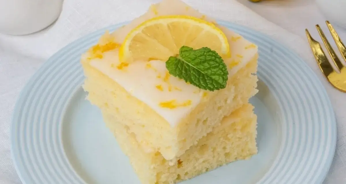Zwei Stücke griechischer Zitronenkuchen mit Joghurt, garniert mit Zitronenscheibe und Minze, auf einem hellblauen Teller.