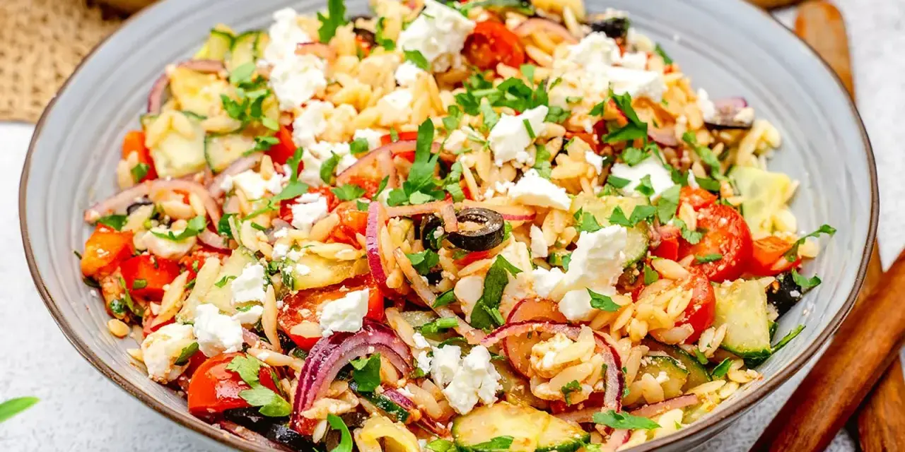 Bunter Kritharaki Salat mit Feta, Tomaten, Gurken, roten Zwiebeln und Oliven, garniert mit Petersilie. Ein köstlicher mediterraner Genuss.