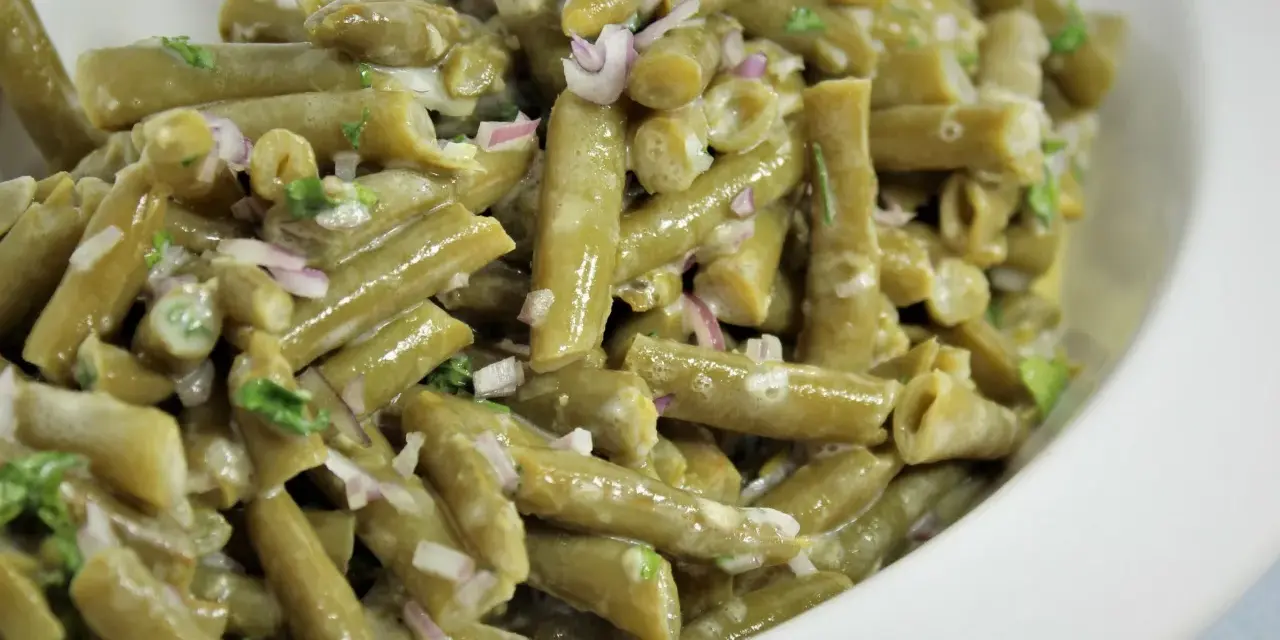 Grüner Bohnensalat mit cremigem Dressing, roten Zwiebeln und Kräutern in einer weißen Schüssel.