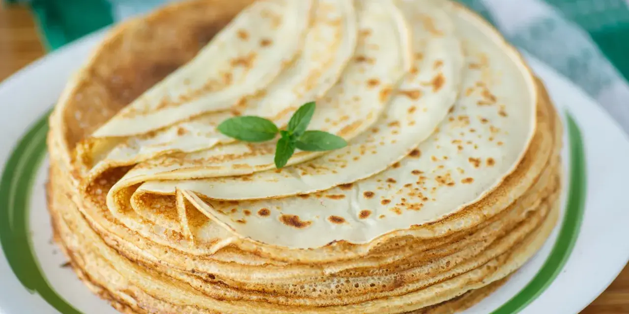 Ein Stapel goldbrauner Pfannkuchen, wie nach Omas Pfannkuchen Rezept, mit einem Minzblatt garniert.