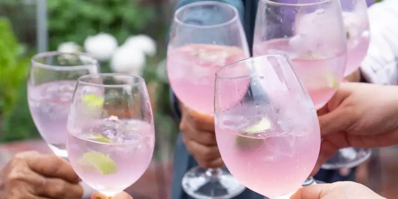 Hände stoßen mit rosafarbenen Sarto Spritz-Cocktails mit Limette und Eis an.