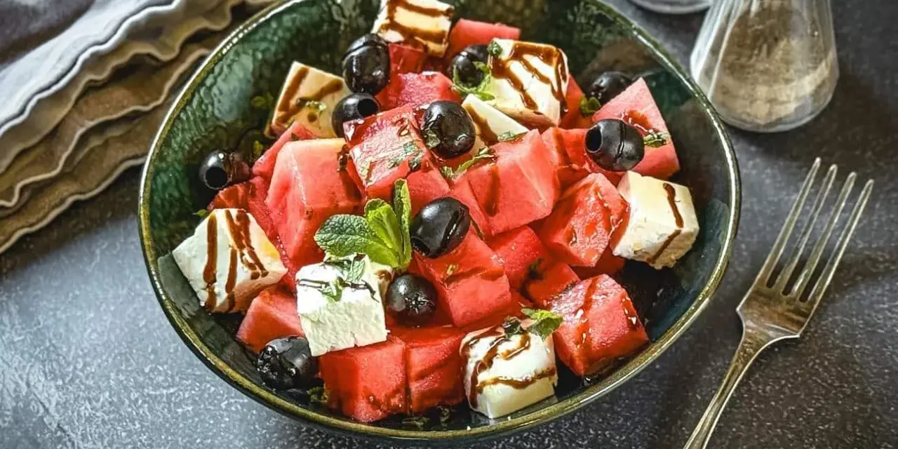 Erfrischender Melone Feta Salat mit schwarzen Oliven und Minze, beträufelt mit Balsamico-Glasur.