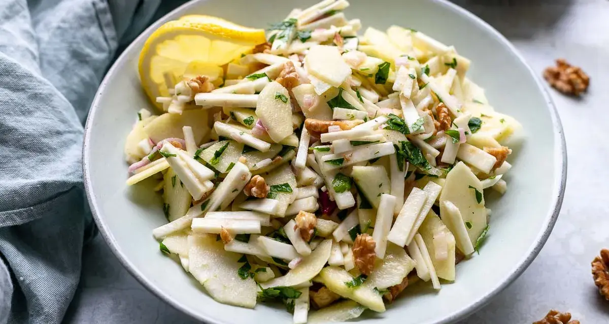 Frischer sellerie salat mit Äpfeln, Walnüssen und Kräutern, garniert mit einer Zitronenspalte.