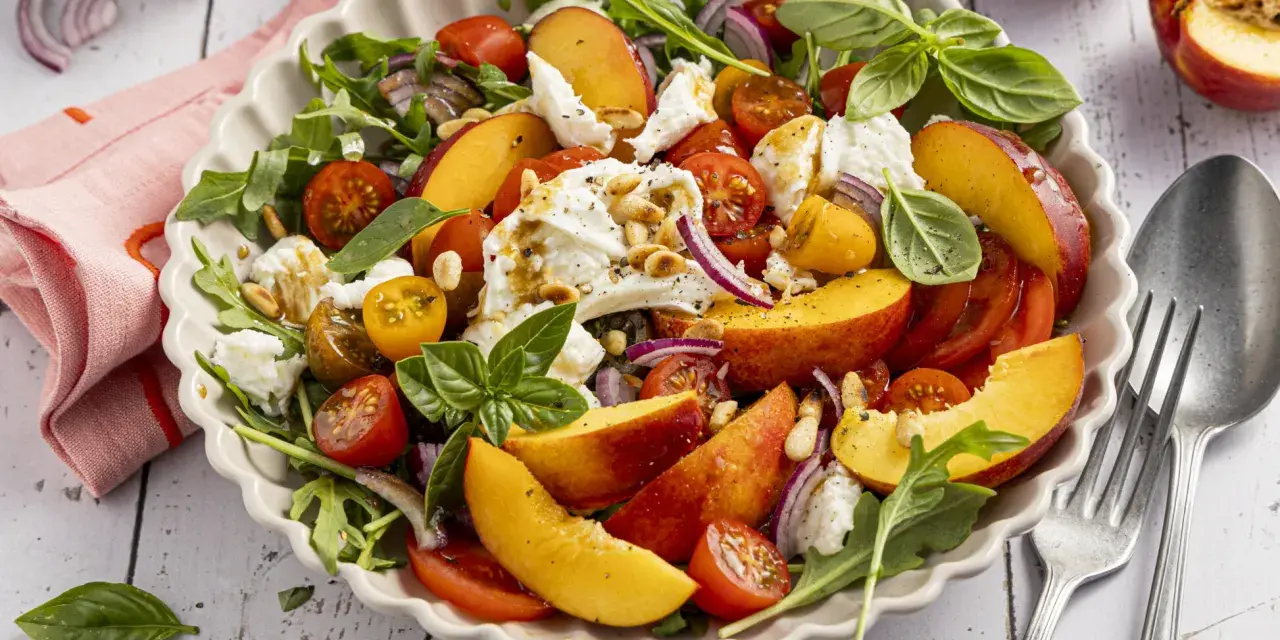 Erfrischender Salat mit saftigen Nektarinen, Tomaten, Mozzarella und Rucola, beträufelt mit Balsamico-Dressing.