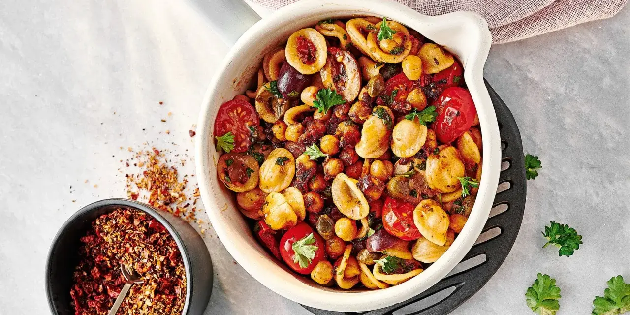 Ein bunter Nudelsalat mal anders: Orecchiette mit Kichererbsen, Kirschtomaten, Oliven und Kräutern in einer Auflaufform. Daneben eine Schale mit Gewürzmischung.