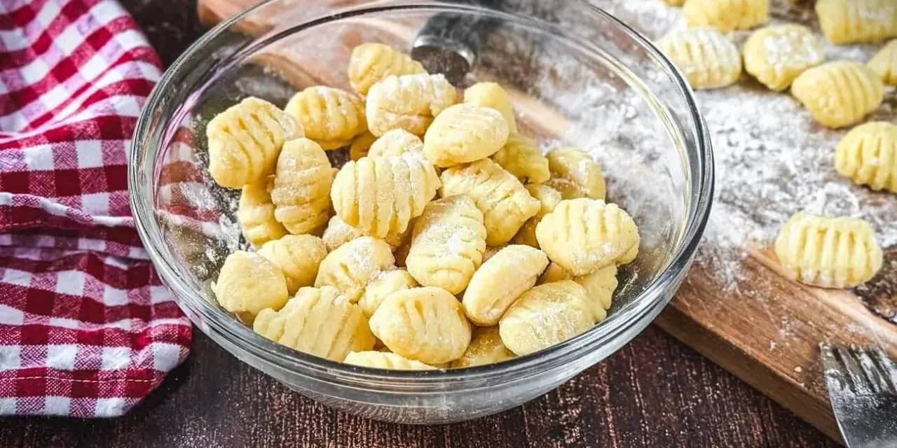 Frisch gemachte Gnocchi in einer Schüssel, bereit zum Kochen. Auf dem Holzbrett liegen weitere Gnocchi, die zeigen, wie einfach es ist, Gnocchi selber machen.