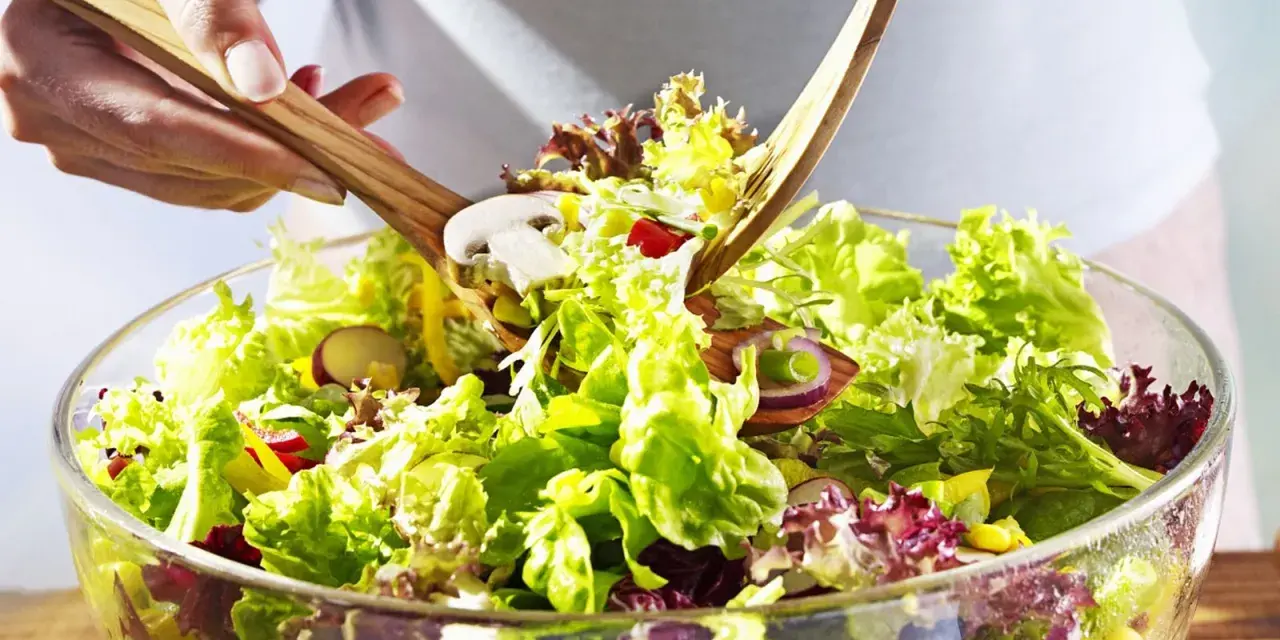 Frischer gemischter Salat mit knackigem Salat, Radieschen, Zwiebeln und Pilzen wird mit Holzsalatbesteck vermischt.
