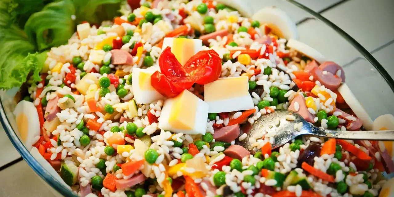 Reissalat mit Erbsen, Karotten, Ei und Wurst – ein gesunder Salat zum Grillen, garniert mit Tomaten und Salatblättern.