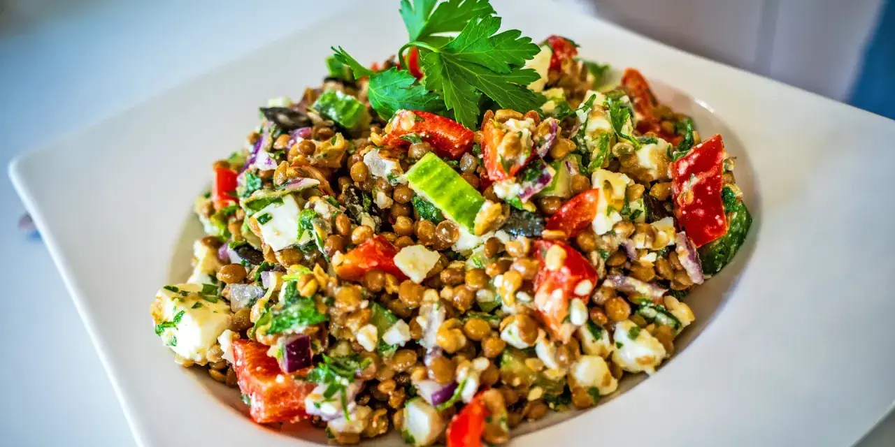 Frischer Linsensalat mit Feta, Paprika, Gurke und Kräutern, garniert mit Petersilie.