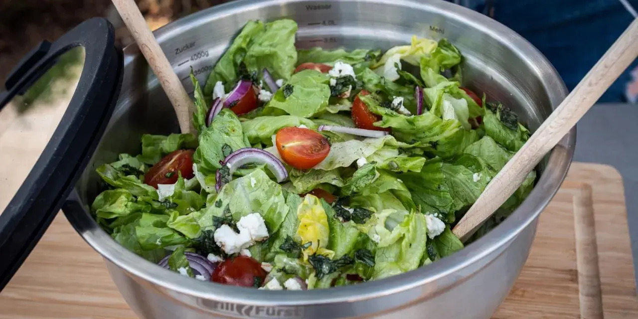 Frischer Salat zum Grillen, zubereitet von Landfrauen. Knackiger Salat mit Tomaten, Zwiebeln und Feta in einer Edelstahlschüssel.