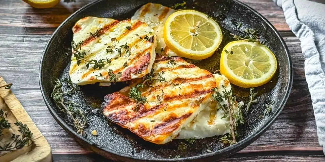 Perfekt gegrillter Halloumi mit Kräutern und Zitronenspalten auf einer Gusseisenplatte. Ein Genuss für alle Sinne!