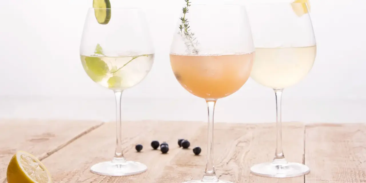 Drei elegante Gläser mit erfrischenden champagner cocktails, garniert mit Limette, Kräutern und Zitrone, stehen auf einem Holztisch.