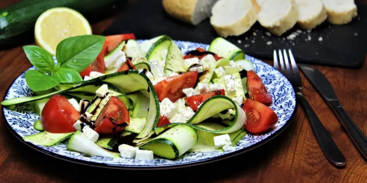Ein erfrischender, sommerlicher Zucchini-Salat mit Tomaten und Feta, garniert mit Basilikum und Balsamico. Dazu Baguettescheiben.