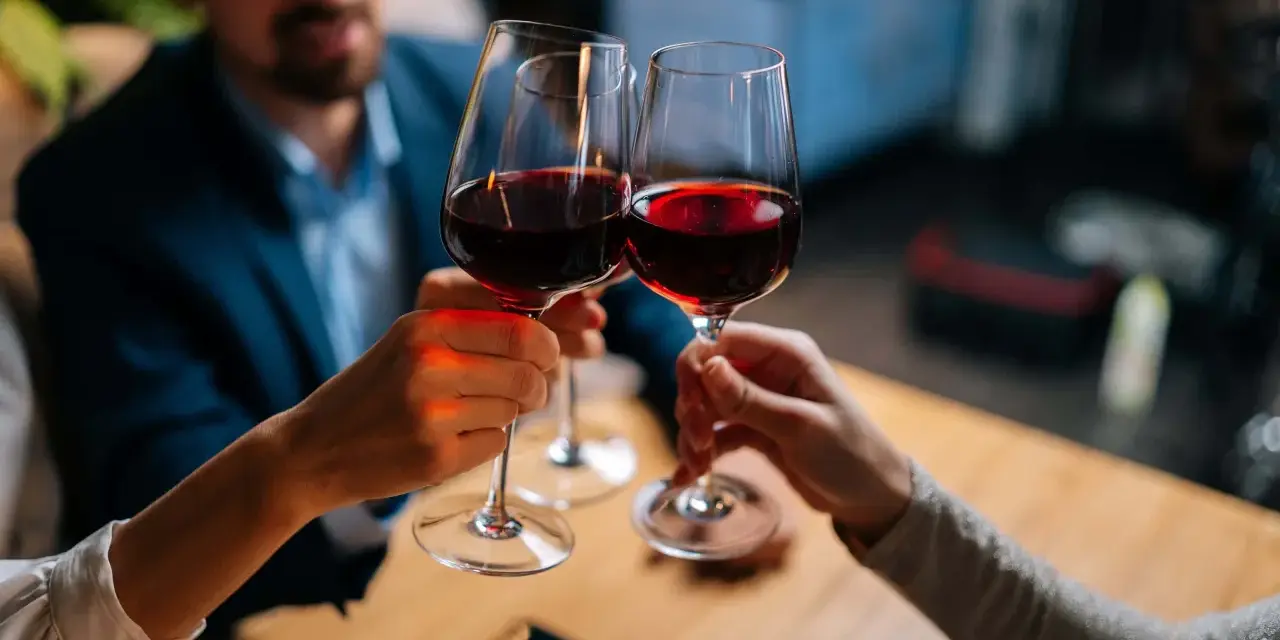 Drei Personen stoßen mit Rotwein an. Sie halten das weinglas richtig, am Stiel, um die Temperatur des Weins zu bewahren.