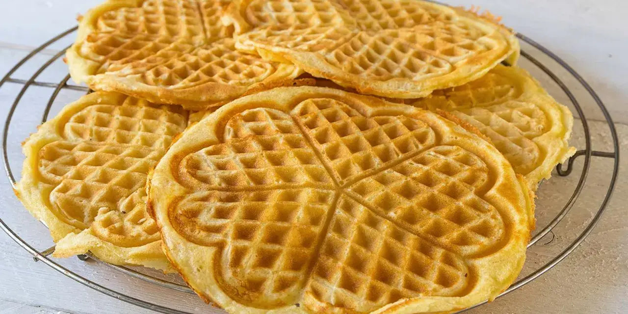 Goldbraune Herz-Waffeln, frisch gebacken aus waffelteig ohne butter, liegen auf einem Gitter.
