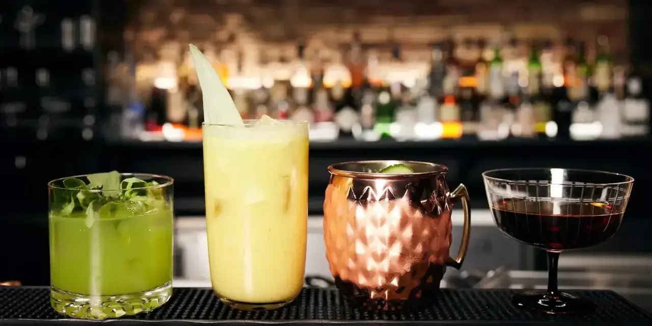 Vier kunstvoll zubereitete Cocktails, die die Definition eines perfekten Drinks verkörpern: ein grüner, ein gelber, ein Moscow Mule und ein dunkler Aperitif.