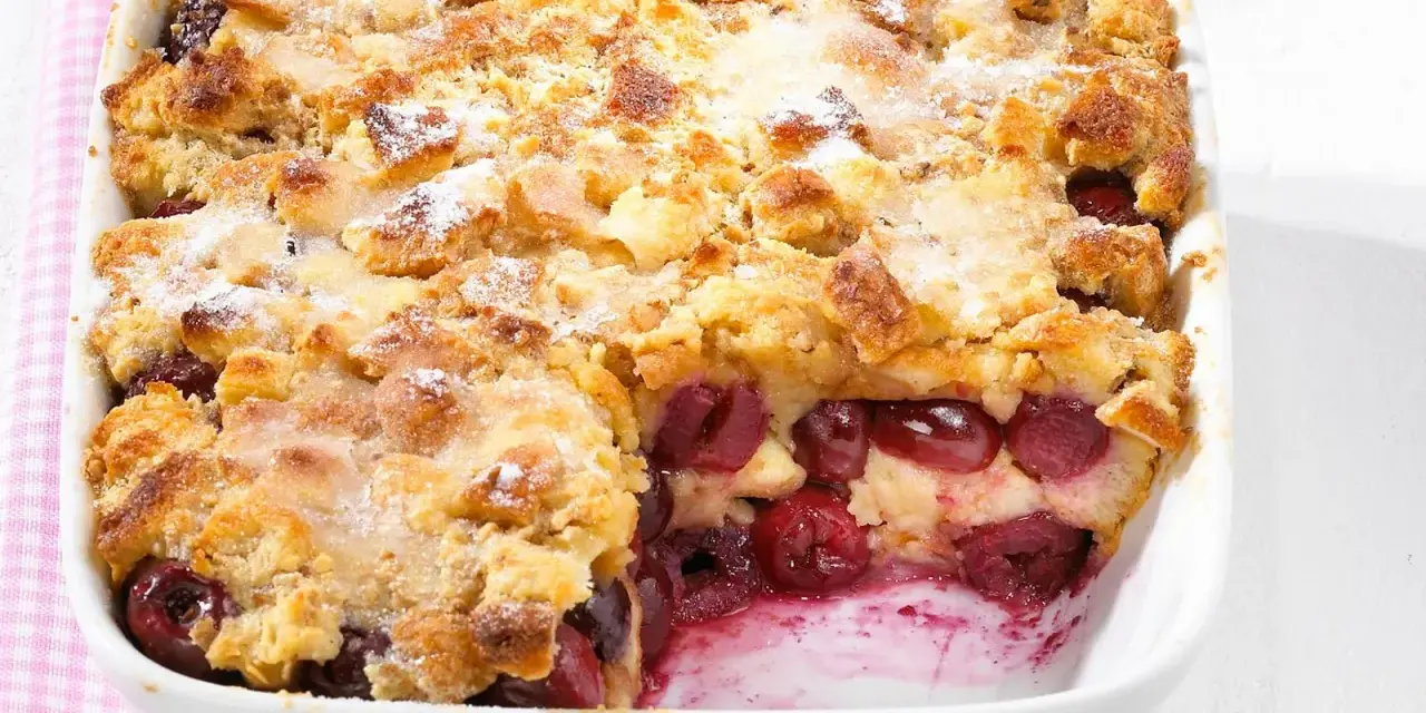Omas Kirschenmichel Rezept: Ein goldbrauner Auflauf mit saftigen Kirschen und knuspriger Streuselhaube, bestäubt mit Puderzucker.
