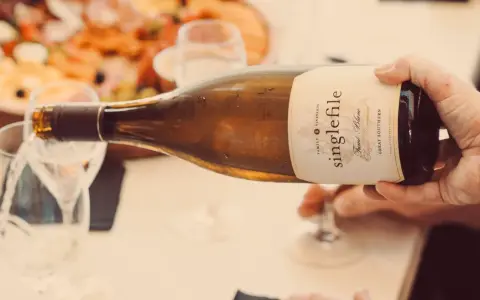 Eine Hand gießt einen **fumé wein** aus einer Flasche in ein Glas. Im Hintergrund ist eine Platte mit Speisen zu sehen.