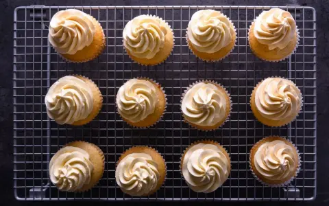 Zwölf Cupcakes mit cremiger deutscher Buttercreme auf einem Gitter.