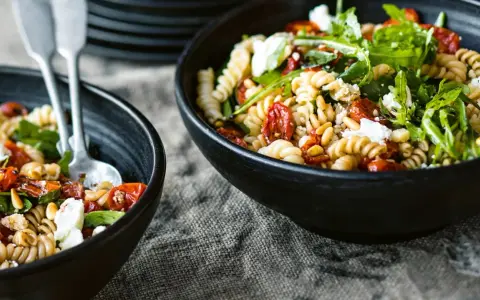 Zwei Schüsseln mit Nudelsalat, perfekt für das Grillen. Fusilli mit getrockneten Tomaten, Rucola und Feta.