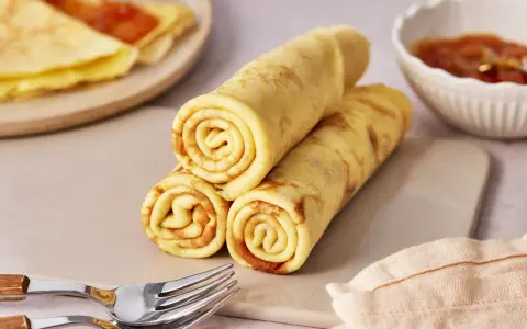 Gestapelte Quark Pfannkuchen, goldbraun gebacken, mit einer Schale Marmelade und Gabeln daneben.