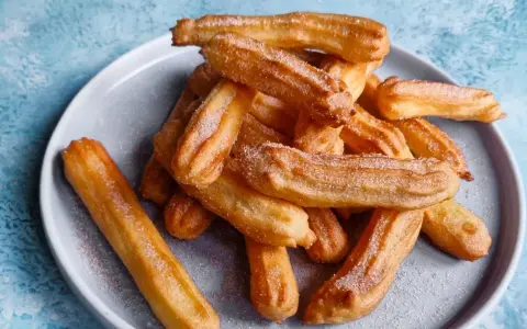 Goldbraune Churros, frisch aus dem Airfryer, mit Zucker bestreut auf einem grauen Teller.