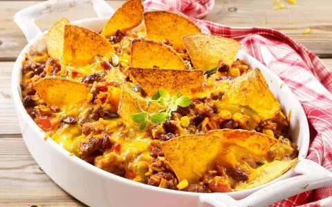 Herzhafter nacho auflauf mit Hackfleisch, Bohnen, Mais und geschmolzenem Käse, garniert mit Tortilla-Chips und frischen Kräutern.