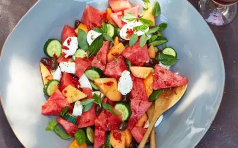 Erfrischender Melonensalat mit Mozzarella, Gurke und Basilikum auf einem grauen Teller.