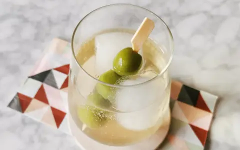 Erfrischender Italicus Spritz mit Eiswürfeln und Oliven auf einem gemusterten Untersetzer.