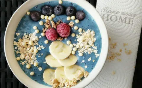 Blauer Smoothie-Bowl mit Blaubeeren, Himbeeren, Bananenscheiben und Granola. Perfekt für gesunde smoothie rezepte.
