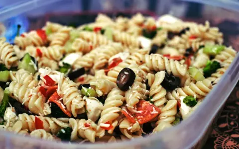 Nudelsalat mit Spiralnudeln, Oliven, Paprika und Brokkoli in einer Plastikschüssel.