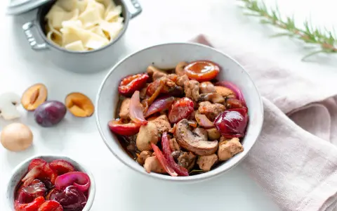 Herzhafte Rezepte mit Pflaumen: Ein Eintopf mit Fleisch, Pilzen und roten Zwiebeln, garniert mit frischen Pflaumen. Daneben eine Schüssel mit Nudeln.
