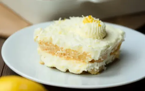 Ein Stück cremiges Limoncello Tiramisu, garniert mit Zitronenzesten und einem Tupfer Sahne, auf einem weißen Teller.