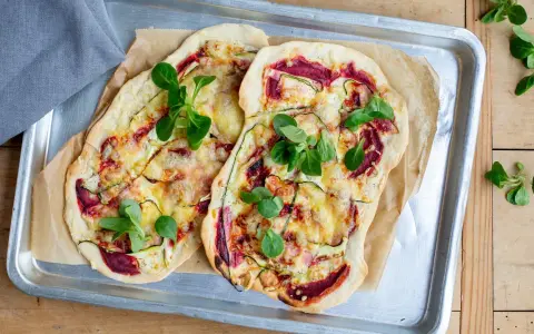 Zwei Flammkuchen mit Zucchini und Roter Bete, garniert mit frischen Blättern. Eine histaminarme Alternative, bei der man auf Weintrauben verzichtet.