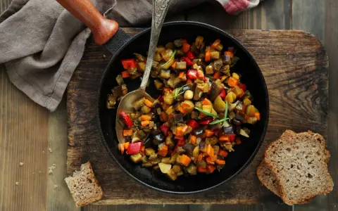 Ratatouille rezept: Buntes Gemüse aus Aubergine, Paprika und Karotten in einer Pfanne, serviert mit Brot.