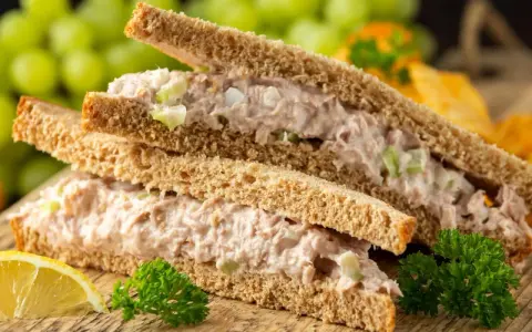 Zwei Tramezzini mit Thunfischsalat, Sellerie und Zwiebeln auf Vollkorntoast. Dazu Trauben, Zitrone und Petersilie. Perfekt für schnelle Tramezzini Rezepte.