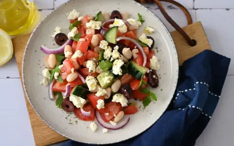 Frischer griechischer Bohnensalat mit Tomaten, Gurken, roten Zwiebeln, Oliven und Feta. Ein Spritzer Olivenöl und Zitrone machen ihn perfekt.