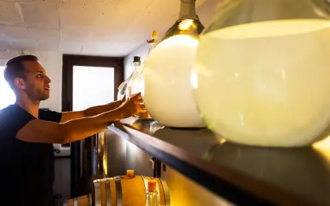 Mann sortiert Flaschen für die Gin-Lagerung. Daneben stehen Fässer und große Glasballons.