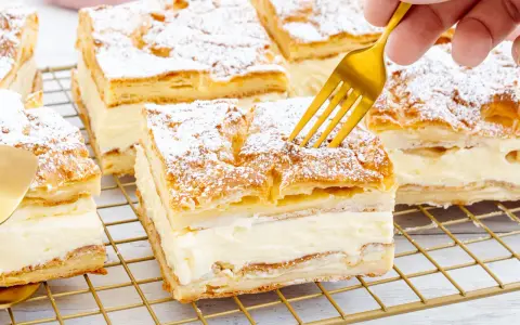 Ein goldener Löffel sticht in ein Stück polnischer Puddingkuchen, bestäubt mit Puderzucker.