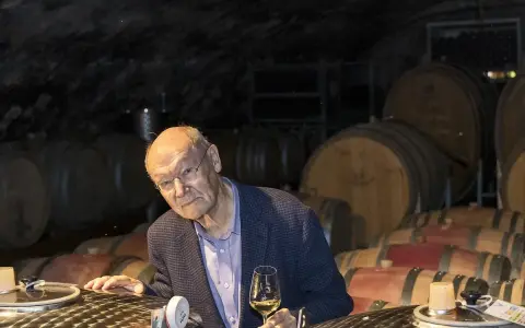 Ein Mann mit Brille hält ein Glas Wein in einem Weinkeller. Die Fässer im Hintergrund und der Wein lassen an Wein und Musik denken.