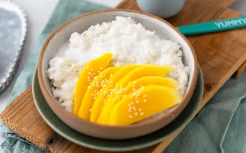 Schüssel mit cremigem **sticky rice** und saftigen Mangoscheiben, bestreut mit Sesam. Ein köstlicher Genuss!